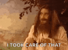 a man with long hair and a beard is standing in front of a tree .