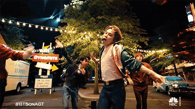 a group of people are dancing on a street in front of a dynamite sign