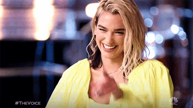 a woman wearing a yellow shirt is smiling and clapping her hands with the hashtag #thevoice