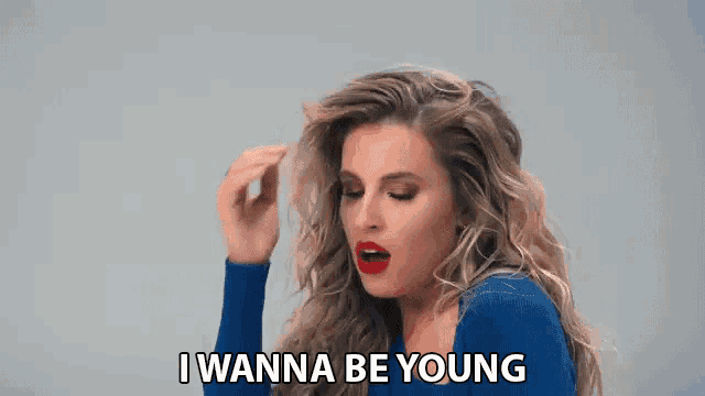 a woman in a blue shirt is holding her hair and says i wanna be young .