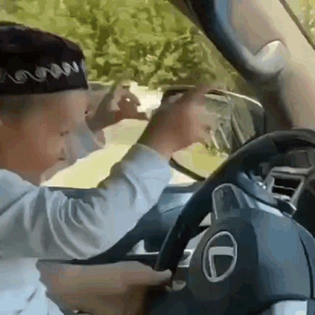 a young boy is sitting in the driver 's seat of a car taking a picture of himself in the rear view mirror .