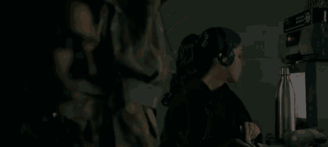 a woman wearing headphones is covering her mouth with her hand in a dark room .