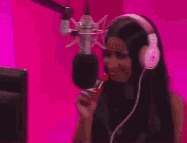 a woman wearing headphones is eating a lollipop in front of a microphone in a pink room .