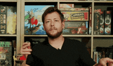 a man smoking a cigarette in front of a shelf full of board games including cuphead
