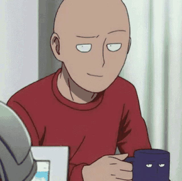 a bald man is sitting at a table holding a blue mug with a face on it .