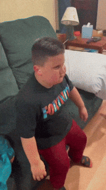 a boy wearing a fortnite shirt sits on a chair