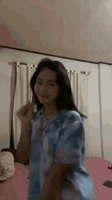 a girl in a blue shirt is dancing on a bed in a room .