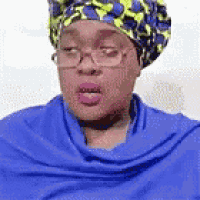a woman wearing glasses , a turban and a blue scarf is making a funny face .