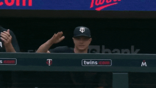 a couple of baseball players sitting in a dugout with a twins logo on the wall
