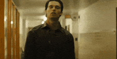 a man walking down a hallway with a red exit sign on the wall