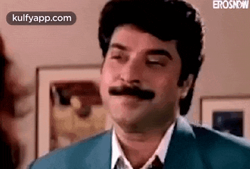a man with a mustache is making a funny face while wearing a suit and tie .