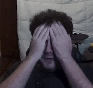 a man is covering his face with his hands while sitting in front of a drum set .
