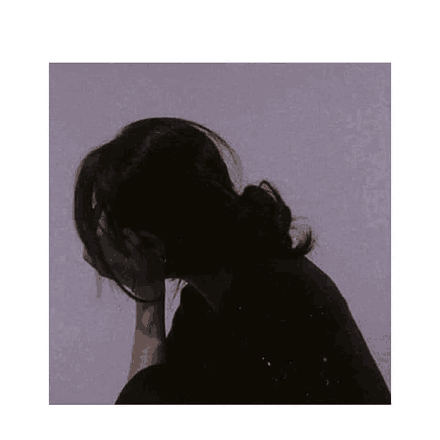 a silhouette of a woman covering her face with her hands against a purple wall .