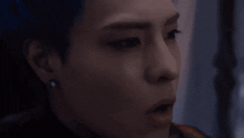 a woman with blue hair and earrings is looking at the camera in a dark room .