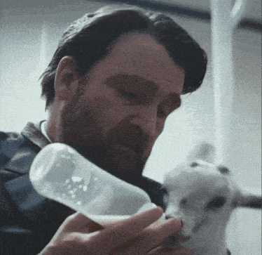 a man feeding a baby goat with a bottle