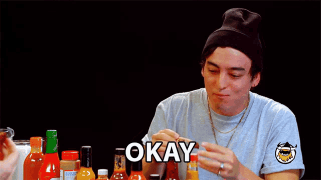 a man sitting at a table with bottles of hot sauce and the word okay on the bottom