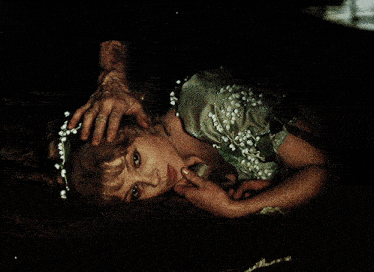 a woman in a green dress with white flowers in her hair is laying on the floor