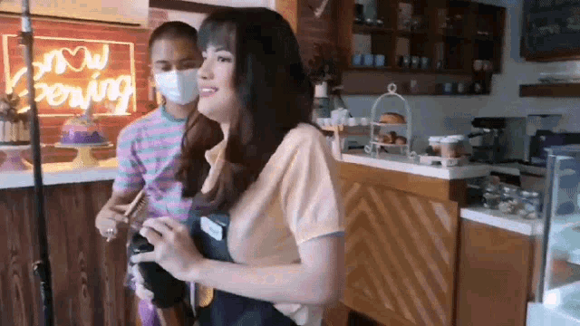 a woman wearing a mask is standing next to a man wearing a mask in a cafe .