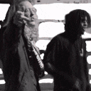 two men are standing next to each other in a black and white photo . one of the men is wearing a supreme hoodie .