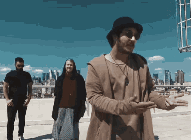 a man wearing a hat and sunglasses stands in front of a city skyline