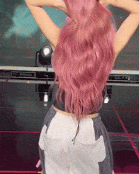 a woman with pink hair is standing on a stage with her hands behind her head