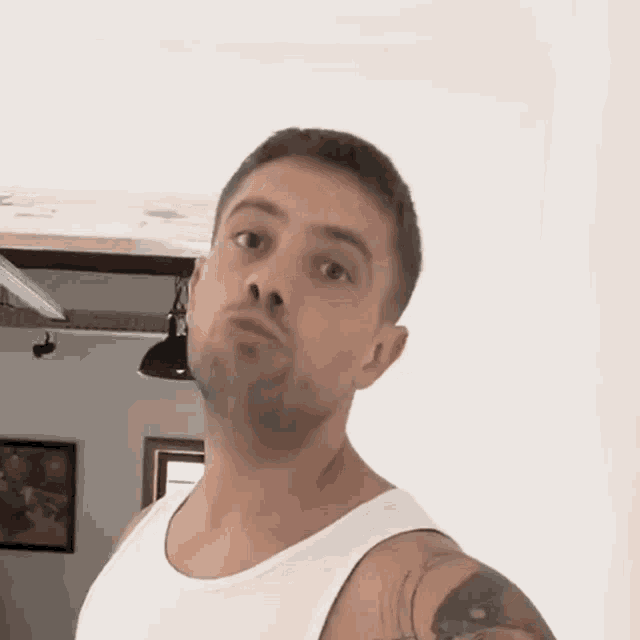 a man wearing a white tank top is making a face