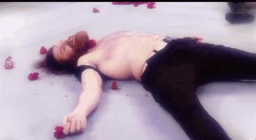a shirtless man is laying on the floor with roses around his head