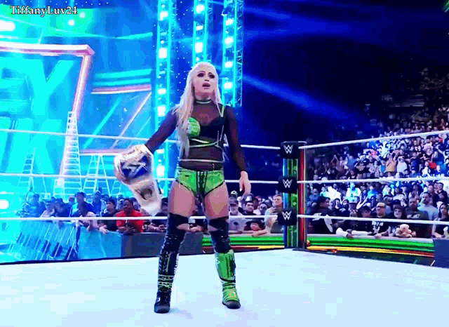 a woman in a green outfit is holding a wrestling glove in a wrestling ring with tiffanyluxe24 written on the screen