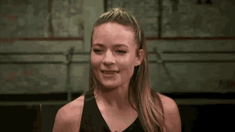 a woman in a black tank top is smiling in a dark room .