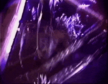 a close up of a person 's face in a dark room with purple lights behind them .