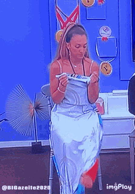 a woman in a white dress is standing in front of a blue wall with gold medals on it