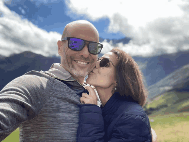 a woman kisses a man on the cheek in front of a mountain