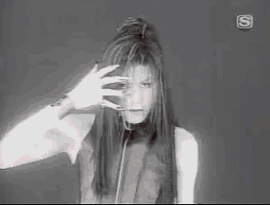 a black and white photo of a woman with long hair making a hand gesture .