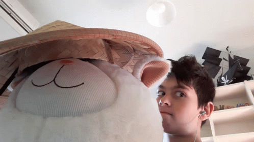 a man wearing ear buds is standing next to a stuffed animal with a hat on it