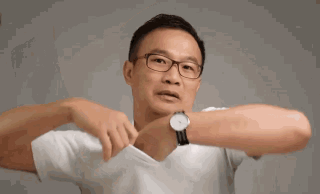 a man wearing glasses and a white shirt is taking off his shirt and pointing at the camera .