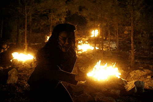 a woman holding a torch in front of a fire