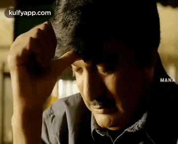 a man with a mustache is touching his forehead with his hand .