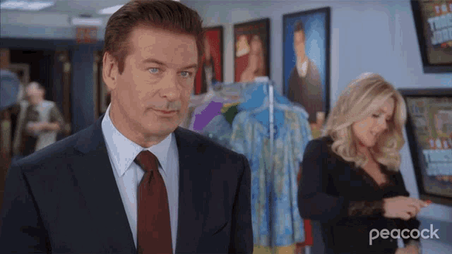 a man in a suit and tie stands in front of a woman in a peacock ad