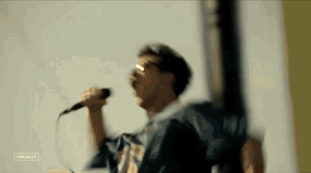 a man is singing into a microphone while wearing sunglasses and a blue jacket .