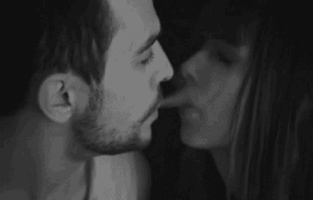 a black and white photo of a man and a woman kissing .