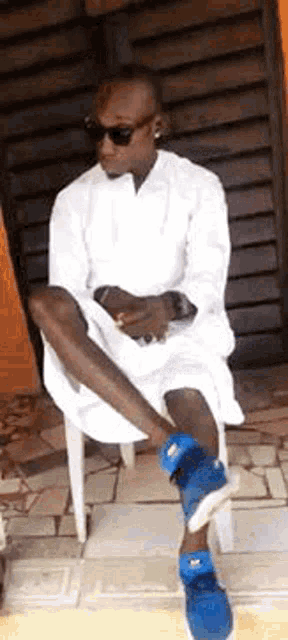 a man wearing sunglasses and a white shirt is sitting on a white chair .