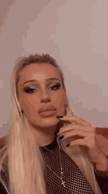 a woman with long blonde hair and black nails is smoking a cigarette and taking a picture of herself .