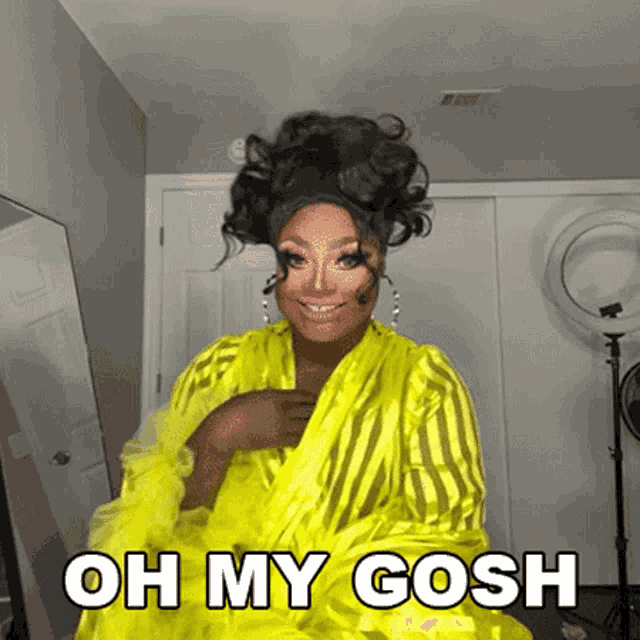 a drag queen is wearing a yellow robe with the words oh my gosh written on it