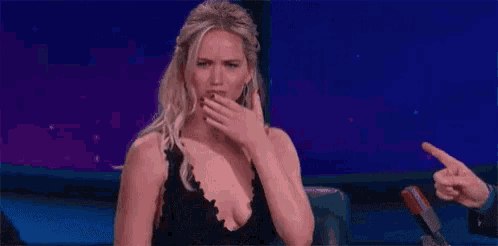 a woman in a black dress is covering her mouth with her hand while a man points at her .