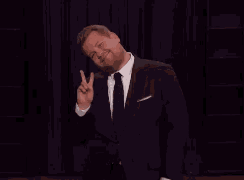 a man in a suit and tie is giving a peace sign while standing on a stage .