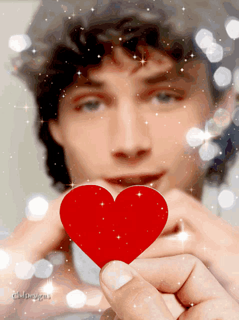 a man is holding a small red heart in front of his face and the word designs is on the bottom right