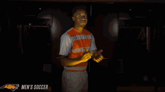 a man stands in a dark room with the words men 's soccer on the bottom right