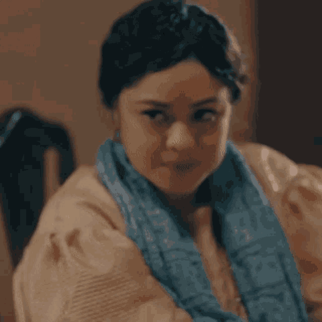 a woman wearing a blue scarf around her neck looks at the camera