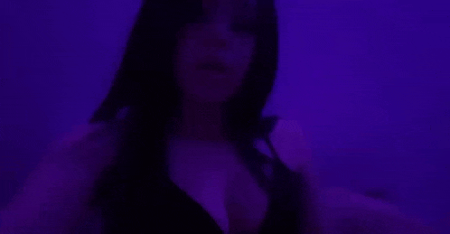 a woman in a black bra is standing in a dark room with purple lights .