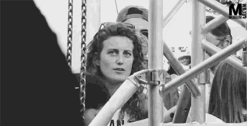 a black and white photo of a woman behind a metal structure with the letter m in the corner